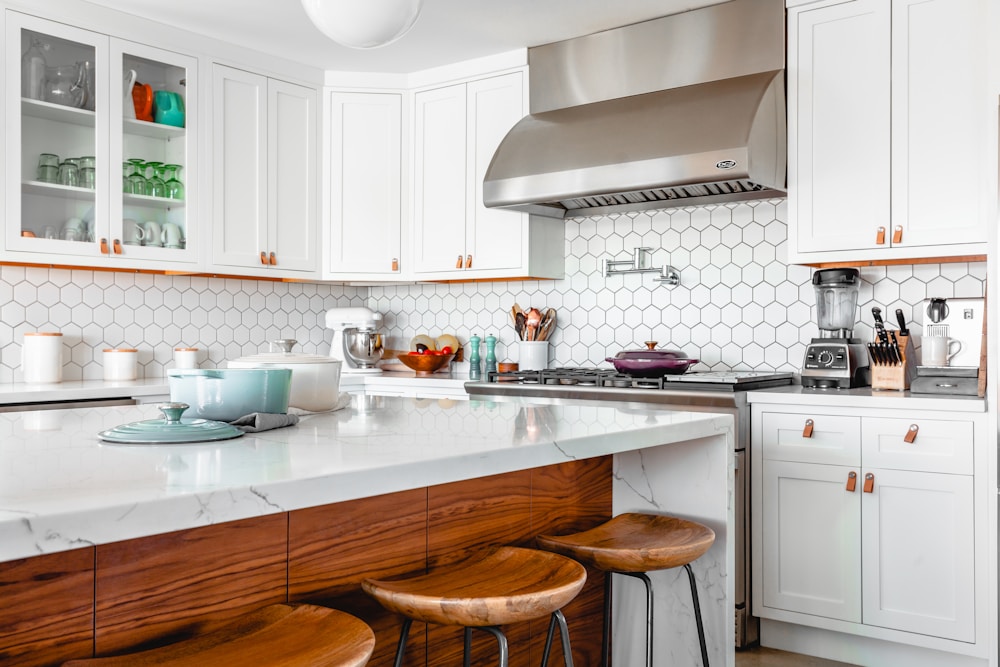 A bright home kitchen with white cabinets, wood stools, and a clear countertop